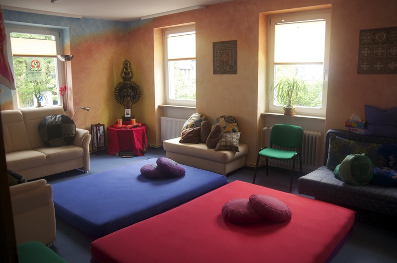 Praxisraum mit Senju-Kannon-Statue, Yoga-Matten in Blau und Rot, Couches und Mandala-Wandbild